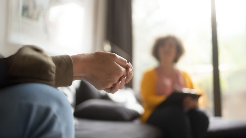 Gabinet terapeutyczny, rozmazana twarz terapeuty, widać tylko ręce klienta.