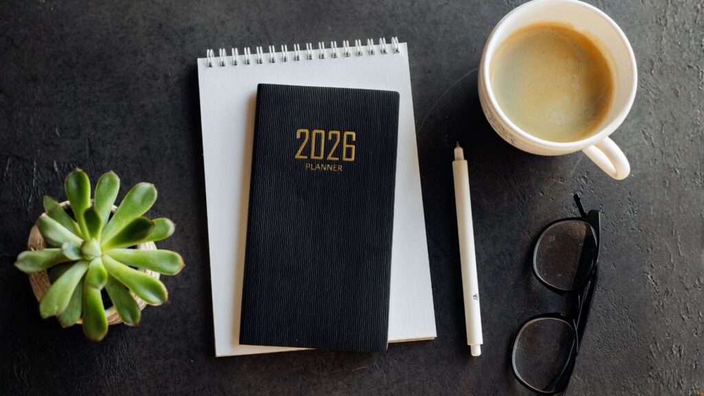 blat biurka z góry, kwiat, notatnik i kalendarz na 2026 oraz kawa, długopis oraz okulary